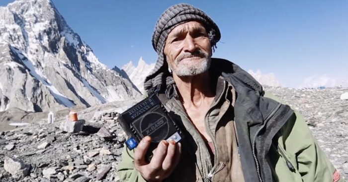 old pakistani man in a head scarf standing in front of a mountain